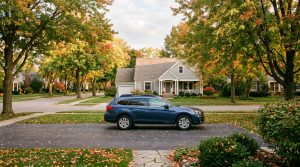 A car parked on a tree-lined residential street with leaves showing seasonal color change