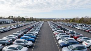 Rows of used vehicles on a dealership lot photographed from an elevated angle under a cloudy sky