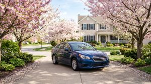 A car parked in a driveway during spring with blooming trees and warm sunlight indicating peak selling season
